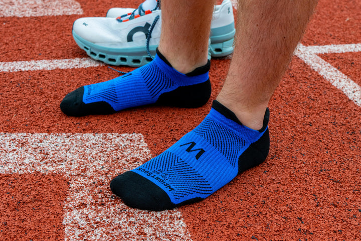 A person standing on a track in Wrightsock Royal Blue Racer Tab socks.