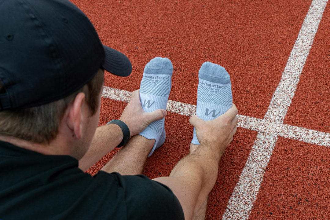 A man stretching on a track wearing Wrightsock Grey Heather Racer Tab socks.